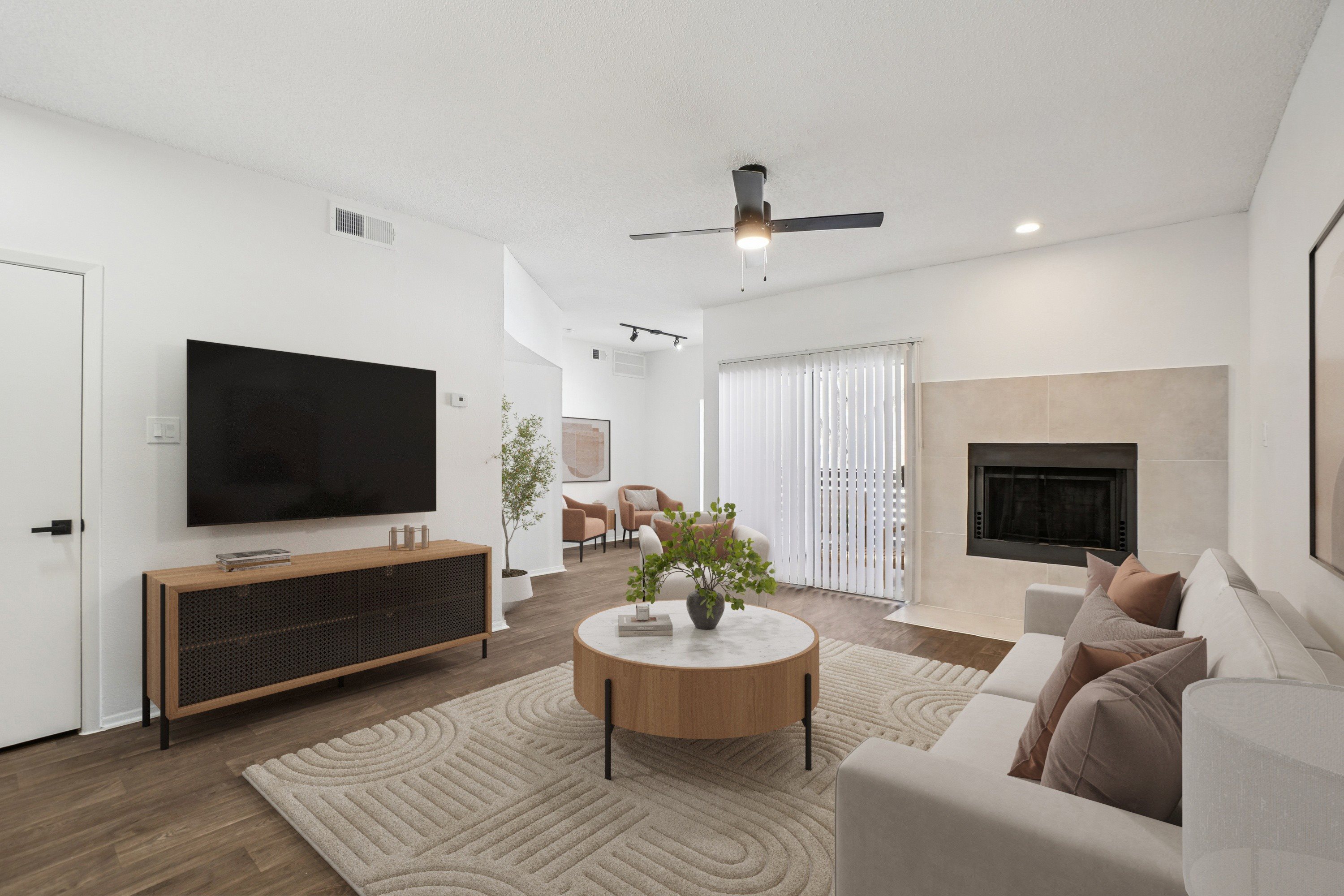 A modern living room with a flat screen TV, a fireplace, and a ceiling fan.